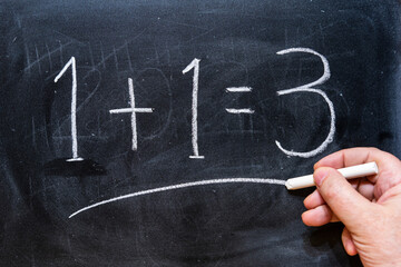 Mano escribiendo con tiza en la pizarra 1 + 1 = 3