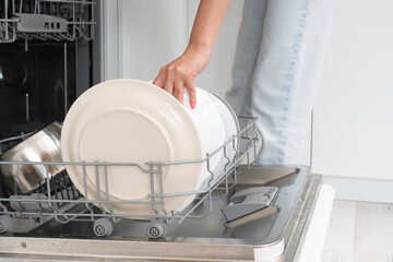 Close-up of female takes of clean dish out of dishwasher machine