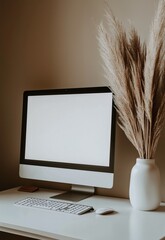 Close-up computer with a blank screen on white desk, boho-style pampas grass in a vase. Minimalist aesthetic, neutral tones, soft light and shadow, beige wall background