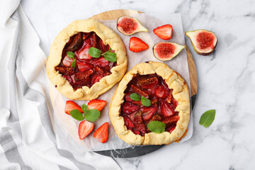 Tasty galettes with strawberries, figs and mint on white marble table, top view