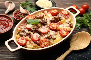 Delicious pasta casserole with cheese, tomatoes and minced meat in baking dish on wooden table, closeup