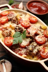 Delicious pasta casserole with cheese, tomatoes and minced meat in baking dish on table, closeup