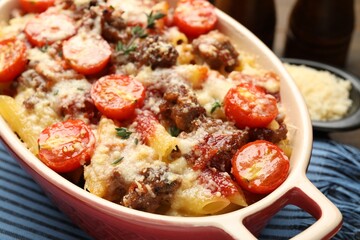 Delicious pasta casserole with cheese, tomatoes, minced meat and thyme in baking dish on table, closeup
