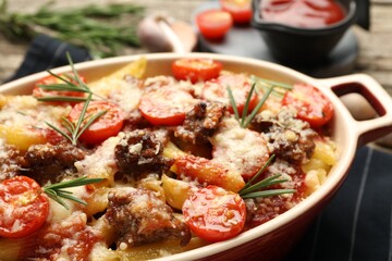 Delicious pasta casserole with cheese, tomatoes, minced meat and rosemary in baking dish on table, closeup