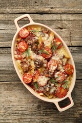 Delicious pasta casserole with cheese, tomatoes, minced meat and rosemary in baking dish on wooden table, top view