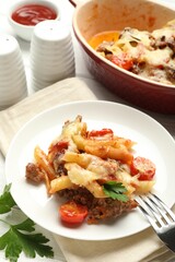 Delicious pasta casserole with cheese, tomatoes, minced meat and parsley on white wooden table