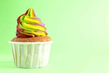 One delicious cupcake with colorful cream on light green background, closeup. Space for text