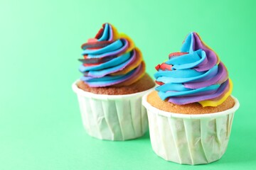 Delicious cupcakes with colorful cream on green background, closeup