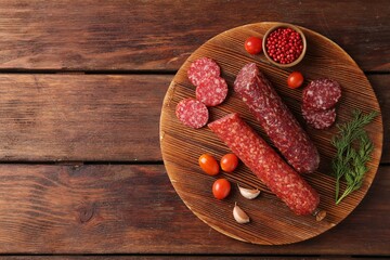 Different smoked sausages, cherry tomatoes and spices on wooden table, top view. Space for text