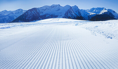 A freshly groomed ski trail in the Alps under a clear blue sky. Perfect for winter sports.