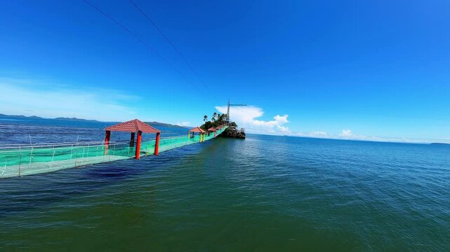 Discover Bacuag Adventure Beach in Surigao Del Norte, Mindanao from above. This aerial tour highlights the hanging bridge to the island, zip lines, zip bikes, and stunning coral reefs in a sunlit trop