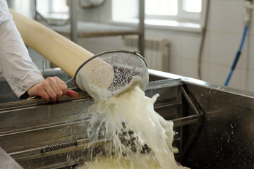 Worker straining liquid through fine sieve in industrial kitchen setup, capturing motion of fluid...