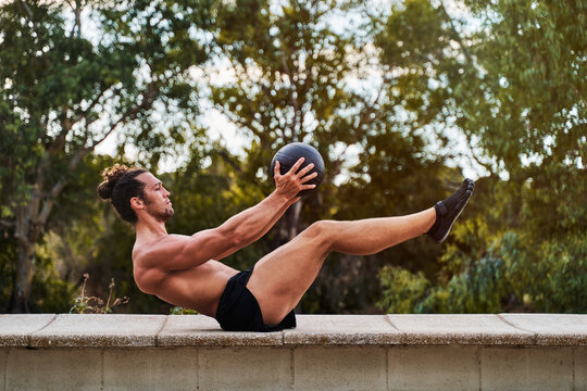 Young man doing sit ups with medicine ball in a park