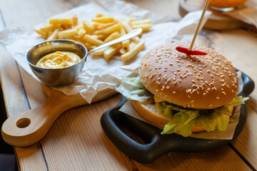 Delicious cheeseburger with french fries and mustard on wooden table