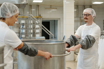 Men in white uniforms and hair nets preparing food in an industrial kitchen. One worker stirring...