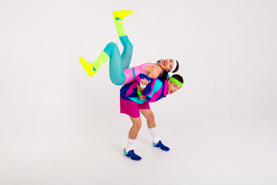 Energetic couple having fun in colorful retro activewear on a grey background, expressing joy and playfulness in a dynamic pose