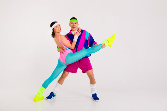 Energetic couple wearing vibrant retro activewear showcasing an impressive dance pose against a minimalistic white backdrop, evoking fun