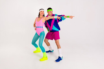 Energetic young couple in retro workout attire pointing ahead with dynamic poses on a white...
