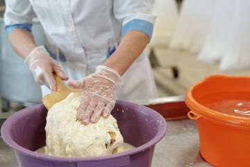 Worker mixing dough manually while wearing gloves in bakery setting, ensuring hygiene and safety during food preparation process