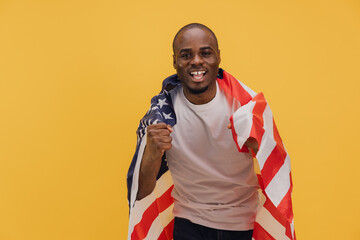 Young african american man celebrating with american flag on yellow background