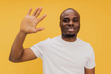 Young african american man waving his hand on yellow background