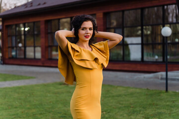 Beautiful young woman in mustard dress standing on a street . Holding her hair up with her hands. Beautiful sunset light.