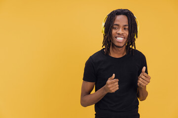 Young man with dreadlocks enjoying music with yellow headphones on yellow background