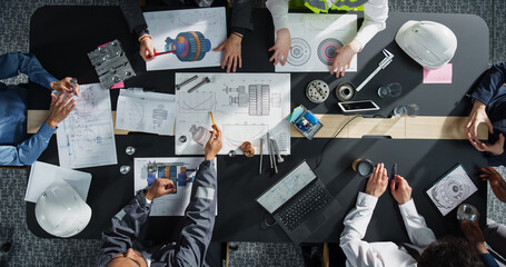 Top Down View of Diverse Team of Business Professionals and Engineers Working Together on Architectural Plans in a Corporate Office. Focused Colleagues Using Laptop, Tablet, Blueprints And Documents