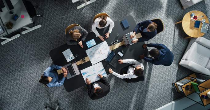 Diverse Professionals Working on Business Statistics Reports and Digital Plans in an Office. Top Down View of Discussion and Data Analysis on Laptops and Charts. Teamwork and Innovation Concept