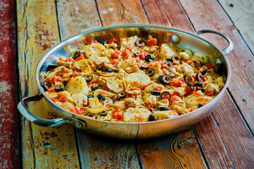 scallop and chicken pasta with garlic, tomatoes and black olives served in a skillet