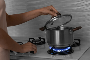 Woman near gas stove with pot in kitchen, closeup