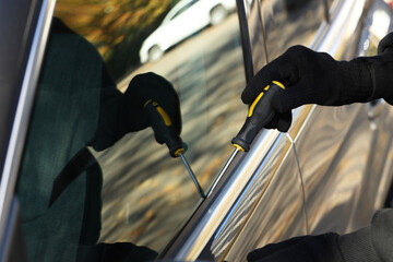 Thief with screwdriver breaking into auto, closeup. Car hijacking
