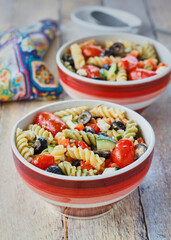 tri-colored pasta salad with cherry tomato, black olives, and feta cheese in red bowls