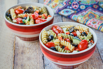 tri-colored pasta salad with cherry tomato, black olives, and feta cheese in red bowls