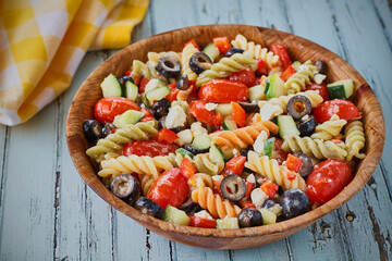 tri-colored pasta salad with cherry tomato, black olives, and feta cheese in a wooden bowl