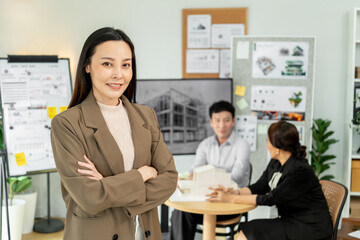 Confident business leader standing with arms crossed while team discusses architectural project in modern office