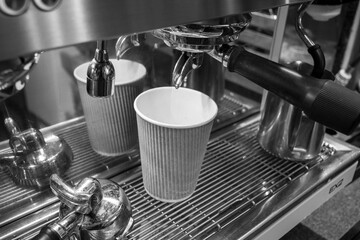 A coffee machine with a cup of coffee pouring out of it. The coffee machine is black and white