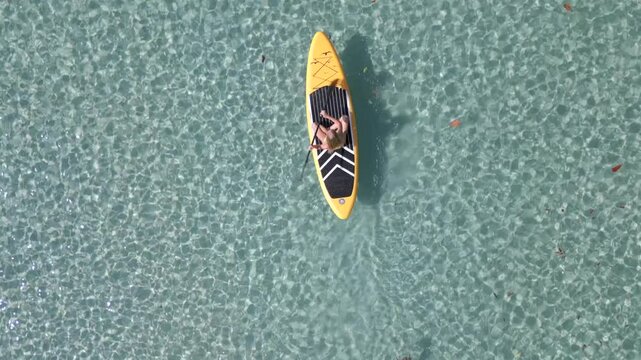 Aerial view of caucasian woman on paddleboard floating in the crystal clear sea in Thailand