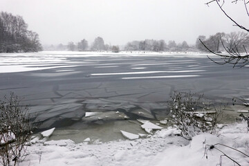 Landscape with frozen broken ice floes on the river in rural place in overcast cold winter day