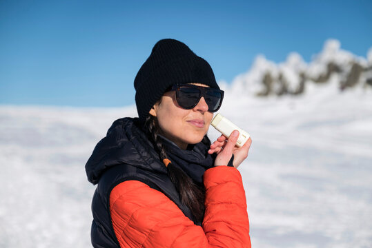 Young woman applying sunscreen stick  in the winter mountain .Spf stick 