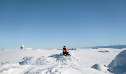 Woman sitting on a stone in the winter snowy mountain 
