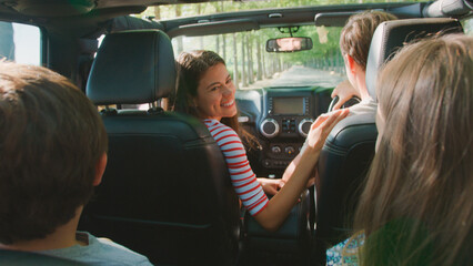 Rear View Of Family On Road Trip In Convertible Car Driving Along Tree Lined Road