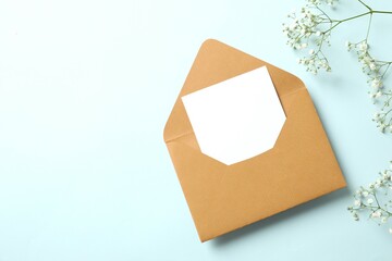 Wedding invitation concept. Top view photo of open envelope with paper card and white gypsophila flowers on pastel blue background with empty space