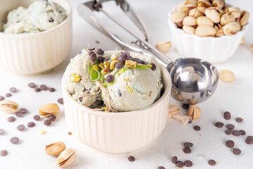 Dubai Chocolate Ice Cream, bowl with pistachio ice cream with tahini, kataifi and chocolate drops, with Dubai chocolate flavored syrup topping and pistachio nuts, on white kitchen table, copy space