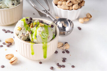 Dubai Chocolate Ice Cream, bowl with pistachio ice cream with tahini, kataifi and chocolate drops, with Dubai chocolate flavored syrup topping and pistachio nuts, on white kitchen table, copy space
