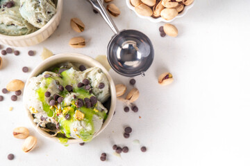 Dubai Chocolate Ice Cream, bowl with pistachio ice cream with tahini, kataifi and chocolate drops, with Dubai chocolate flavored syrup topping and pistachio nuts, on white kitchen table, copy space