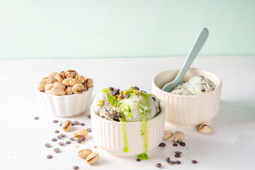 Dubai Chocolate Ice Cream, bowl with pistachio ice cream with tahini, kataifi and chocolate drops, with Dubai chocolate flavored syrup topping and pistachio nuts, on white kitchen table, copy space
