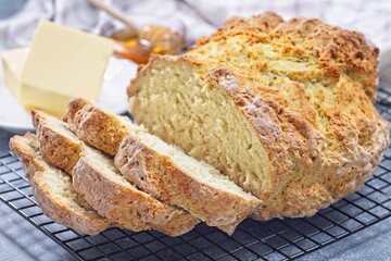Freshly baked soda bread on cooling rack, sliced, butter and honey in the background, horizontal
