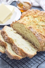 Freshly baked soda bread on cooling rack, sliced, with butter and honey in the background, vertical