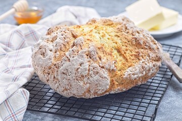 Freshly baked soda bread on cooling rack with butter and honey in the background, horizontal